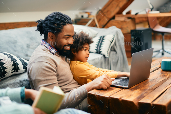 African American father having fun while surfing the net on laptop with his daughter at home. - Stock Photo - Images