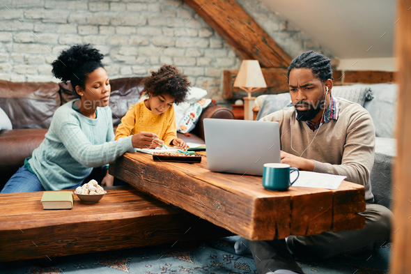 African American man working on laptop while being with his family at home. - Stock Photo - Images