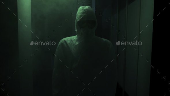 Man in protective suit and mask stands in dark. Stock footage. Creepy doctor in antiviral suit