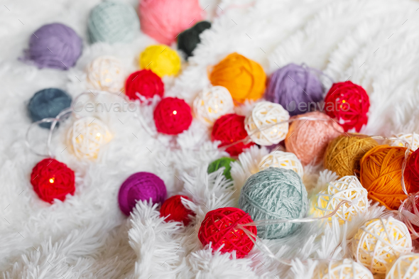 A lot of multicolored knitting yarn and a luminous garland lie on fluffy blanket.