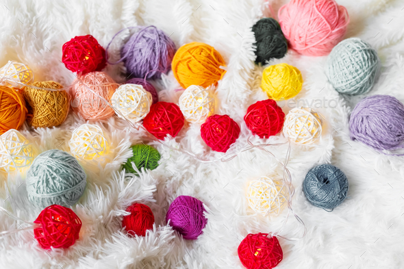 Bright multicolored knitting yarn and a luminous garland in the form of balls lie on fluffy blanket.