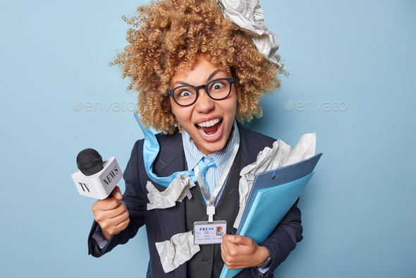 Crazy female reporter shouts loudly poses with folders and microphone going to take interview ready