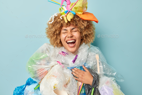 Joyful funny woman laughs happily collects plastic rubbish to stop problem of pollution covered with