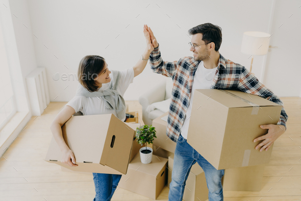 Happy woman and man celebrate moving to new apartment, pose in empty room with cardboard boxes - Stock Photo - Images