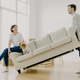 Indoor shot of funny family couple furnish their first home, carry big white sofa - PhotoDune Item for Sale