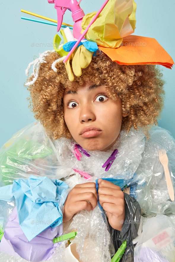 Vertical shot of shocked displeased adult woman with curly hair covered with plastic garbage worried - Stock Photo - Images
