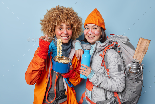 Camping together. Two happy female friends have picnic in forest eat delicious noodle and drink hot - Stock Photo - Images