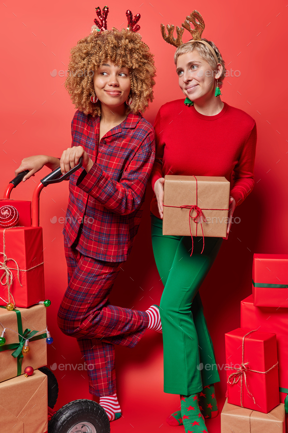 Vertical shot of happy pleased dreamy women pose with wrapped gift boxes prepare for Christmas - Stock Photo - Images