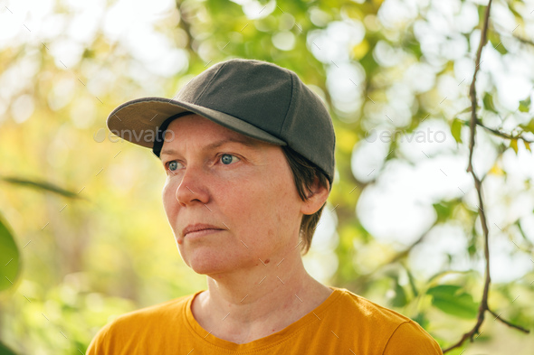 Portrait of female farm worker wearing orange t-shirt and trucker's hat in walnut tree orchard - Stock Photo - Images