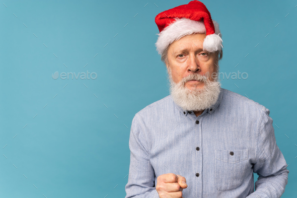 Studio portrait of white beard old man in Santa hat showing fist and looking at camera with angry