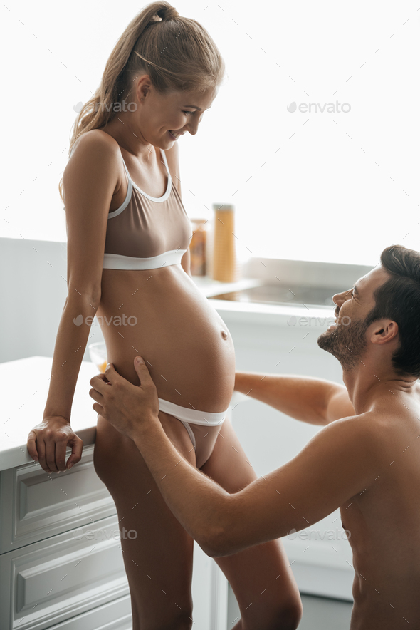 side view of man hugging pregnant wife in underwear in kitchen at home Stock  Photo by LightFieldStudios