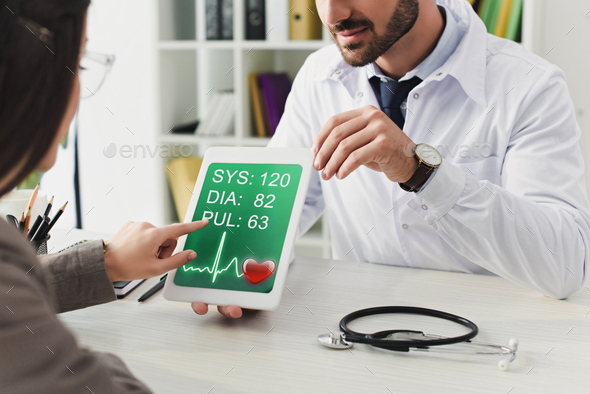 cropped image of doctor showing patient tablet with pulse appliance in clinic