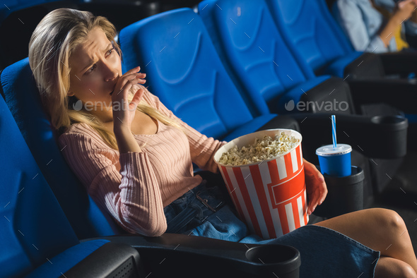 young emotional woman with popcorn watching film alone in cinema