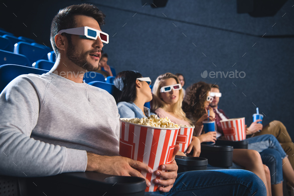 selective focus of multiethnic friends in 3d glasses with popcorn watching film together in movie
