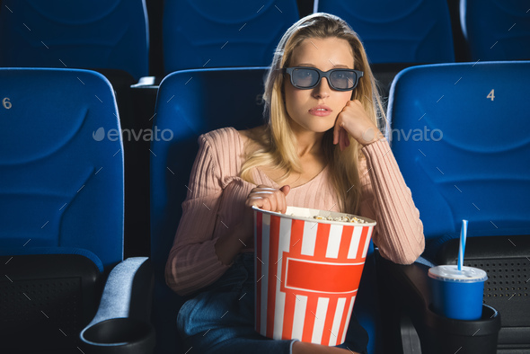 portrait of focused woman in 3d glasses with popcorn watching film alone in cinema