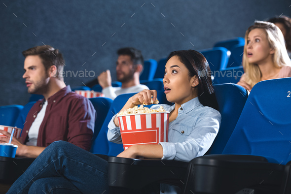 shocked asian woman with popcorn watching movie in cinema alone