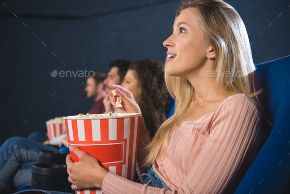 emotional multiethnic friends with popcorn watching film together in movie theater