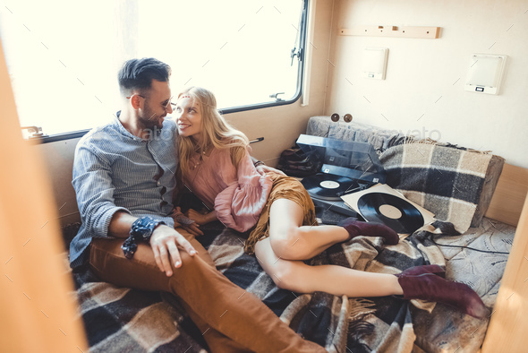 beautiful hippie couple relaxing inside campervan and listening vinyl records