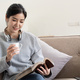 Young beautiful asian woman student sitting on sofa reading book at home while using laptop for - PhotoDune Item for Sale