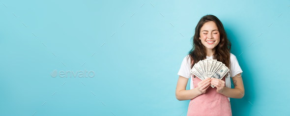 Portrait of cute girl smiling with satisfaction, holding money and looking pleased, winning prize