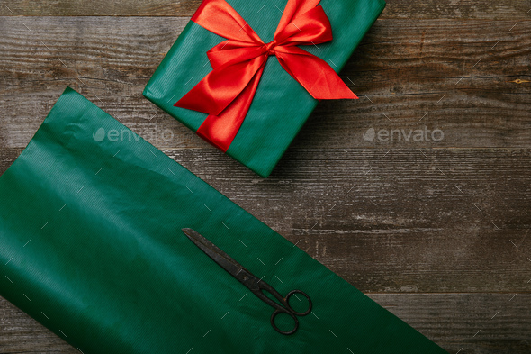 top view of green wrapping paper, scissors and present with red