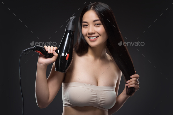 portrait of smiling asian woman with hair dryer looking at camera isolated on black - Stock Photo - Images