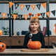 portrait of smiling kid at tabletop with pumpkins and hanging happy halloween flags behind at home - PhotoDune Item for Sale