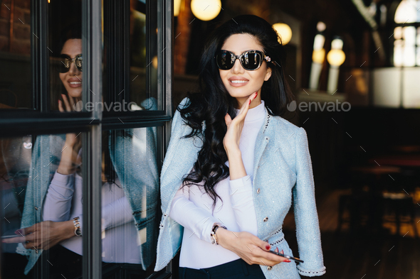 Portrait of glamour young woman with dark wavy hair wearing sunglasses and white blouse - Stock Photo - Images