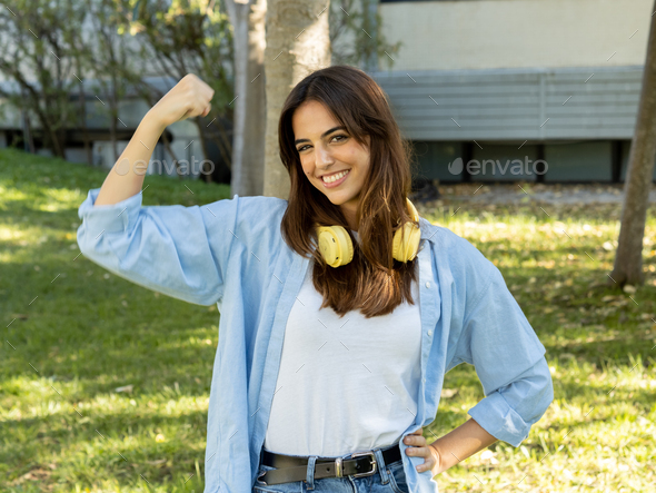 Young smiling woman looking at camera showing biceps. Feminism, female empowerment