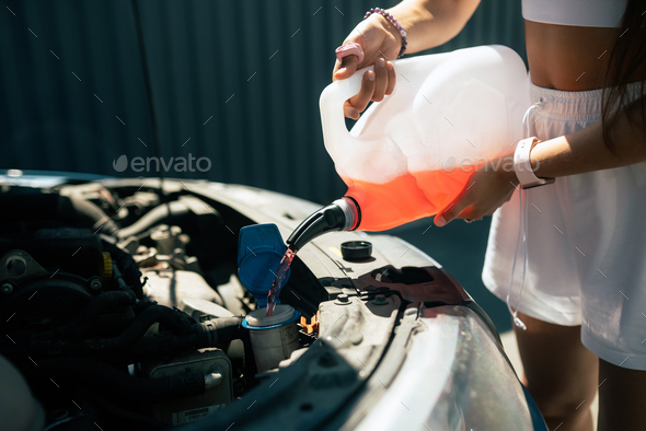 Young woman pouring antifreeze car screen wash liquid into car