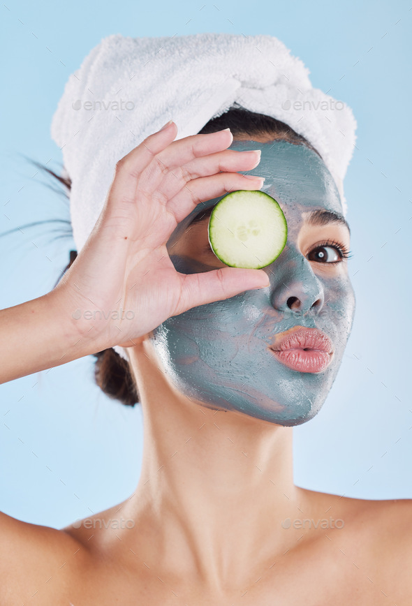 Beautiful young mixed race woman wearing a face mask peel and towel while holding cucumber slices.