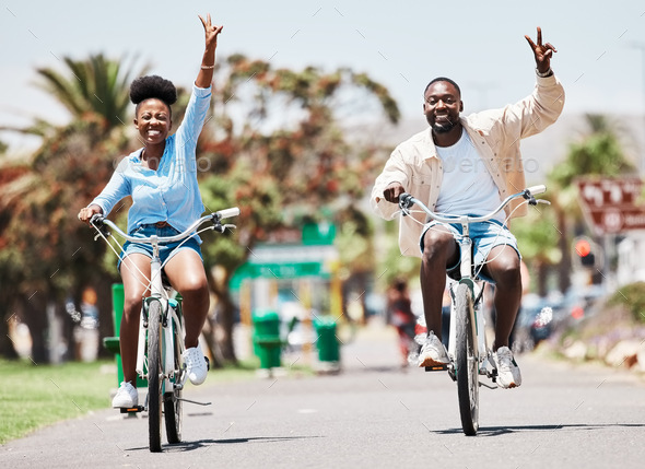 African couple cycling on bike on vacation, peace hand sign on bicycle for sustainable lifestyle in