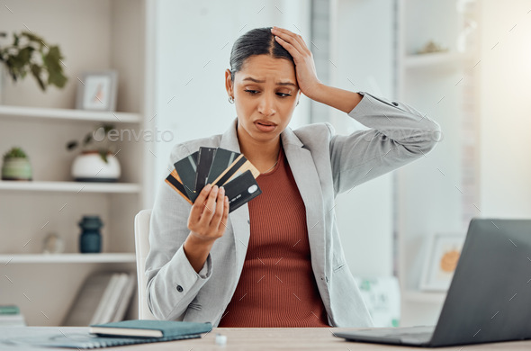 Financial stress, concerned and frustrated woman holding bank cards in her hand at her desk. Busine