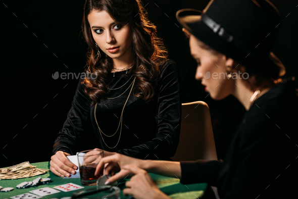 attractive girls playing poker at table in dark room in casino
