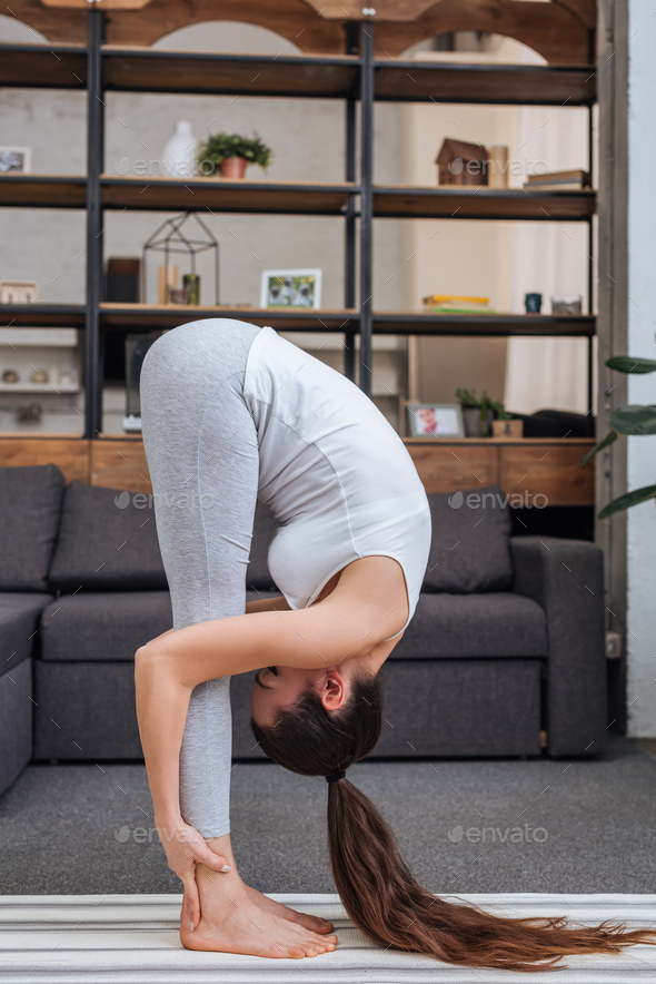 young woman practicing standing forward bend pose at home in living room