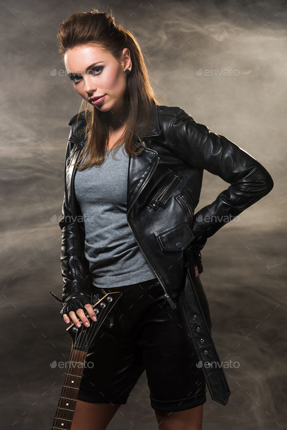 beautiful woman in leather jacket posing with electric guitar on smoky ...