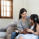 happy asian woman reading a book to daughter embracing her at home. sitting on sofa - PhotoDune Item for Sale