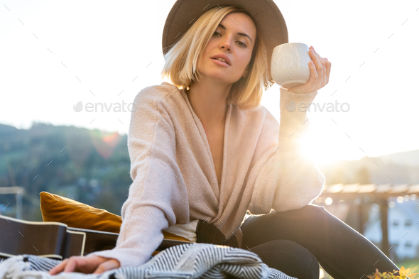 Beautiful woman in cowboy hat drinking coffee on patio in front of her house