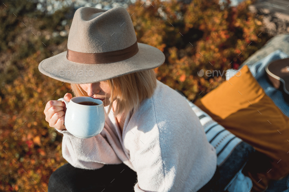 Beautiful woman in cowboy hat drinking coffee on patio in front of her house