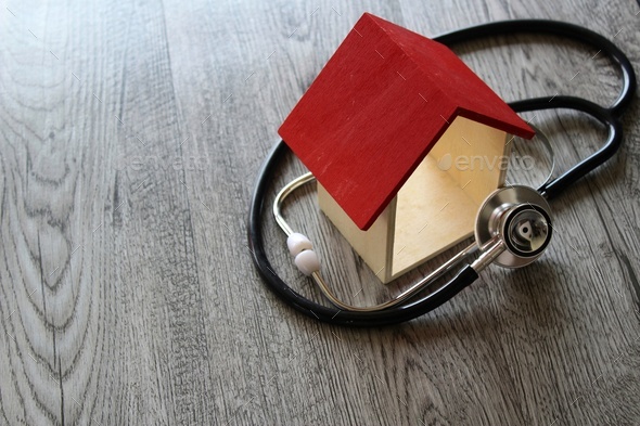 Stethoscope and house on wooden table.