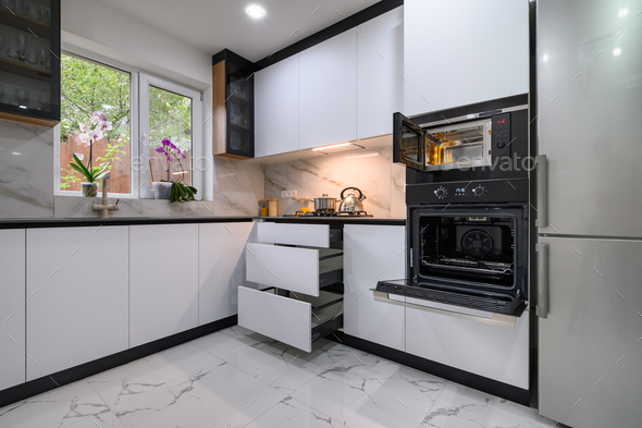 A beautiful kitchen with a white and marble design, a marble floor, an open oven door, and pull-out