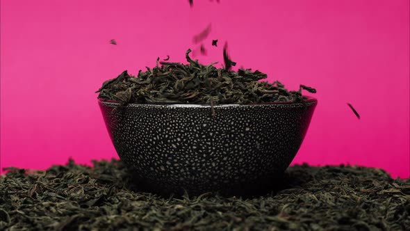 Closeup of Falling Down Dried Tea Leaves Into Black Bowl on Pink Background alt