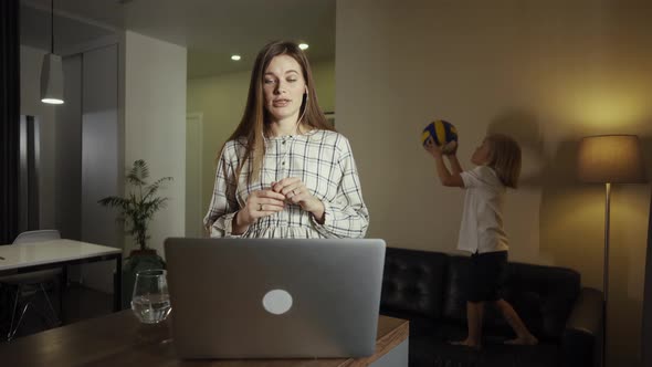 Female Working From Home, Having a Video Call with Colleagues. Kid Playing Ball in the Background.