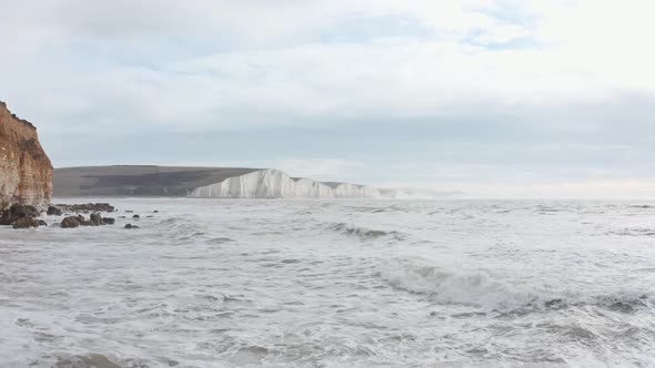 Slow drone shot over rough high tide towards seven sisters cliffs South England alt