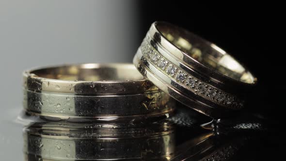 Wedding Rings on Black and White Water Surface Shining with Light. Close Up alt
