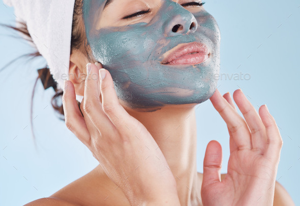 Beautiful young mixed race woman applying a face mask peel isolated in studio against a blue backgr