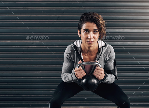 You got this. Shot of a young fit woman using a kettlebell against a black background.