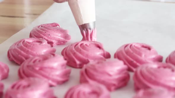 Squeezing pink cream out of a baking bag to make dessert, close up