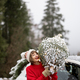 Woman carries wrapped Christmas tree near car in mountains - PhotoDune Item for Sale