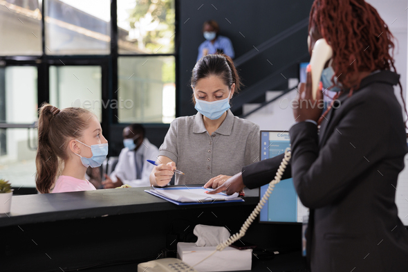 Kid waiting mother to sign medical insurance papers standing at reception desk during checkup visit - Stock Photo - Images